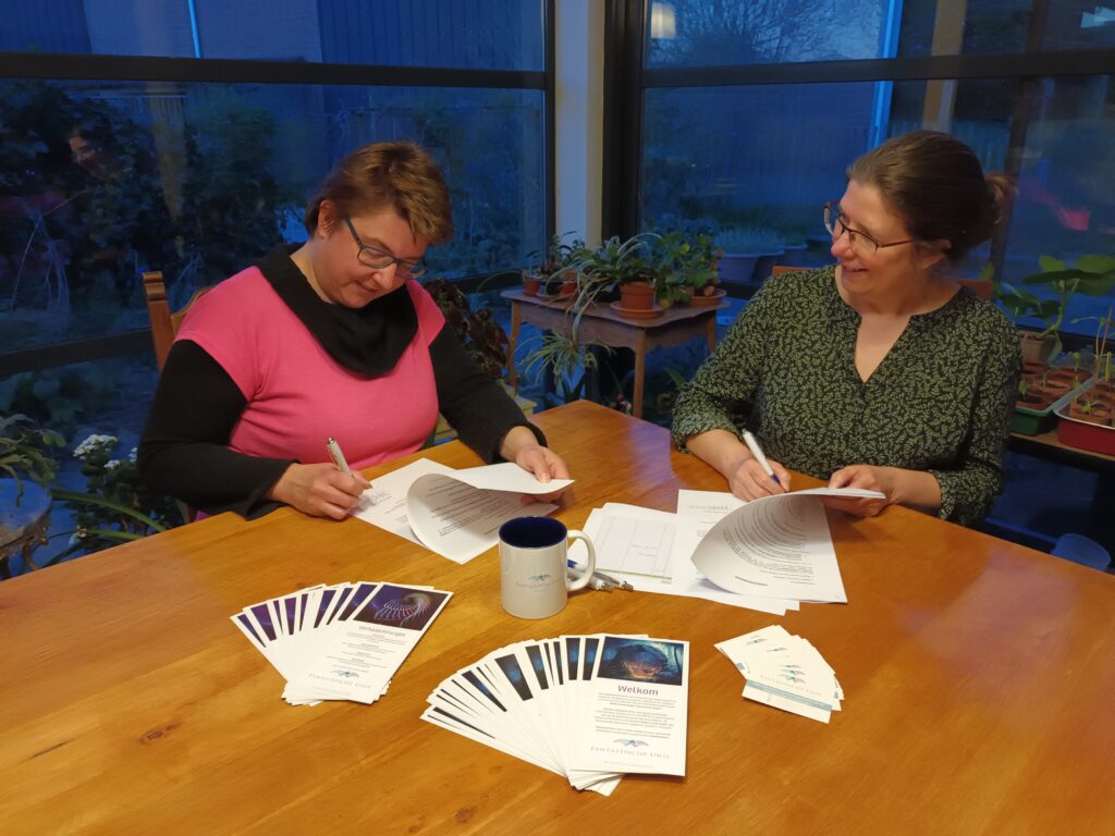 Twee vrouwen zitten aan een tafel en ondertekenen papieren