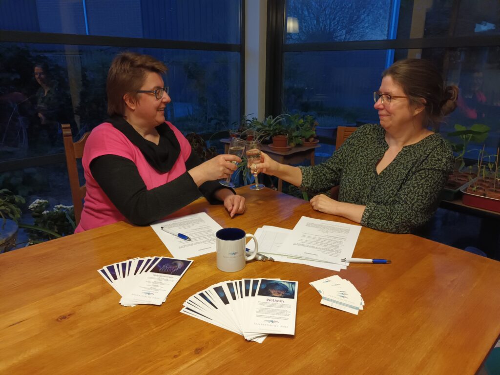 Twee vrouwen zitten aan een tafel en proosten met een glas champagne