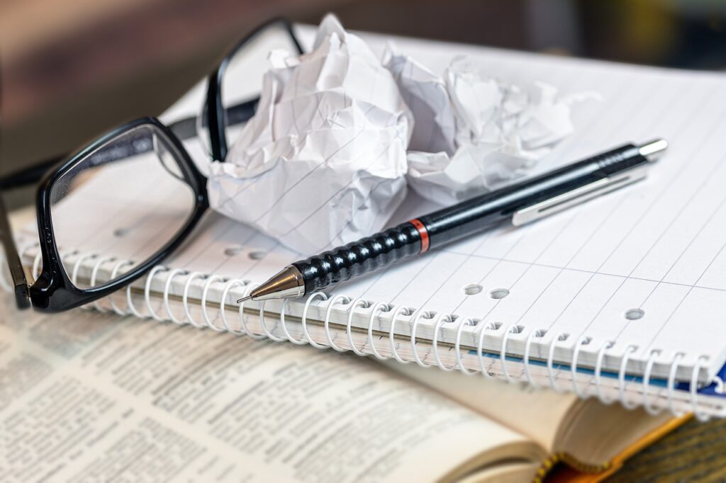bril, prop papier, pen, notiteblok en woordenboek
