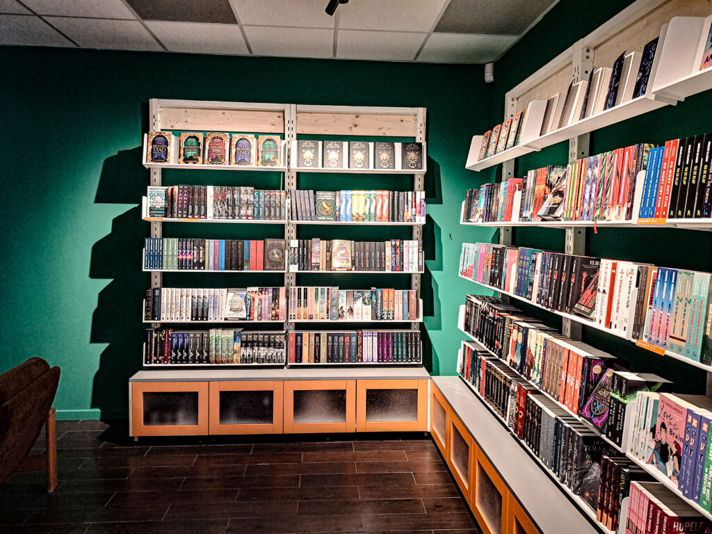 Boekwinkel met boekenrekken rechts en recht vooruit. Groene achterwand.