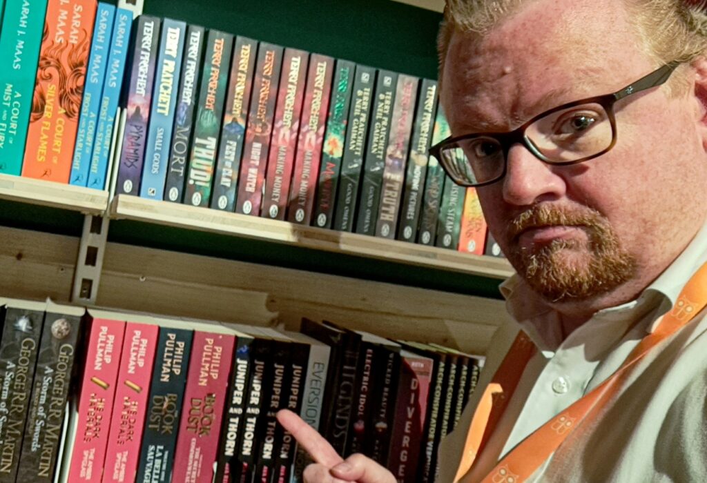 Portret van man met bril die wijst naar boeken in een boekenkast