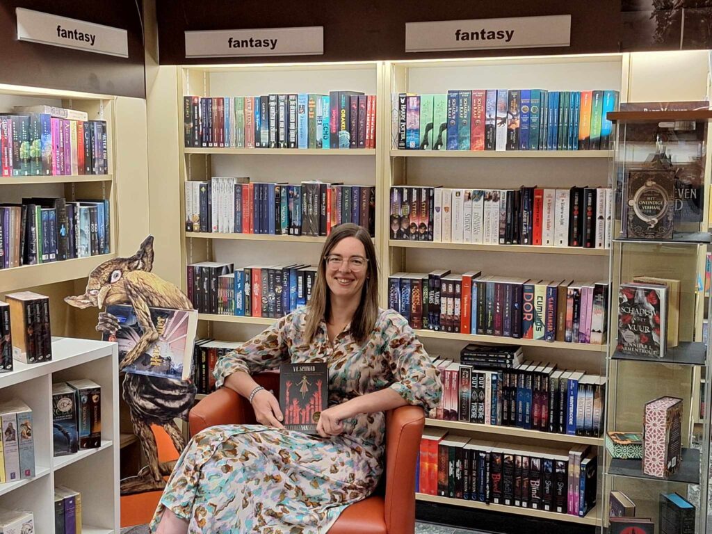 vrouw met bril en boek op schoot zit in een stoel voor een boekenkast